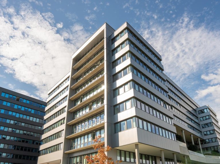Moderne Bürogebäude bei strahlendem Sonnenschein, blauer Himmel mit Wolken im Hintergrund.