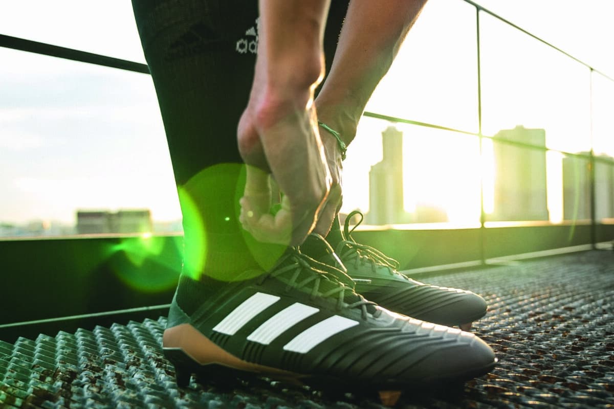 Person schnürt Sportschuhe auf einem Gitter am sonnigen Morgen.