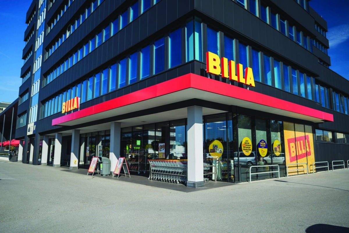 Eckgebäude eines Supermarkts mit BILLA-Logo, große Glasfassaden und Einkaufswagen vor dem Eingang.