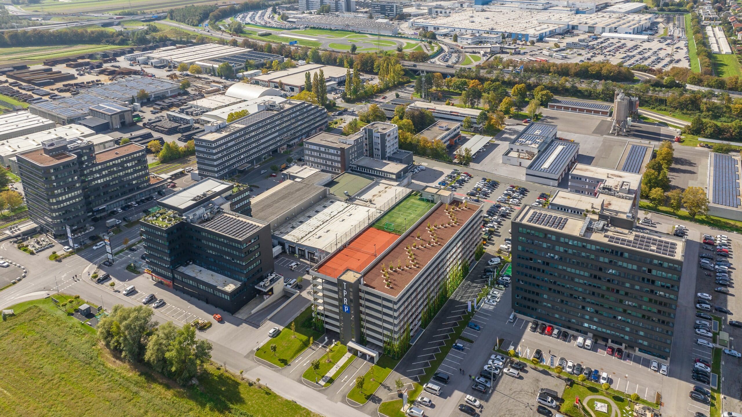 Luftaufnahme des Technopark Raaba mit Bürogebäuden, Parkplätzen und umliegender Landschaft.