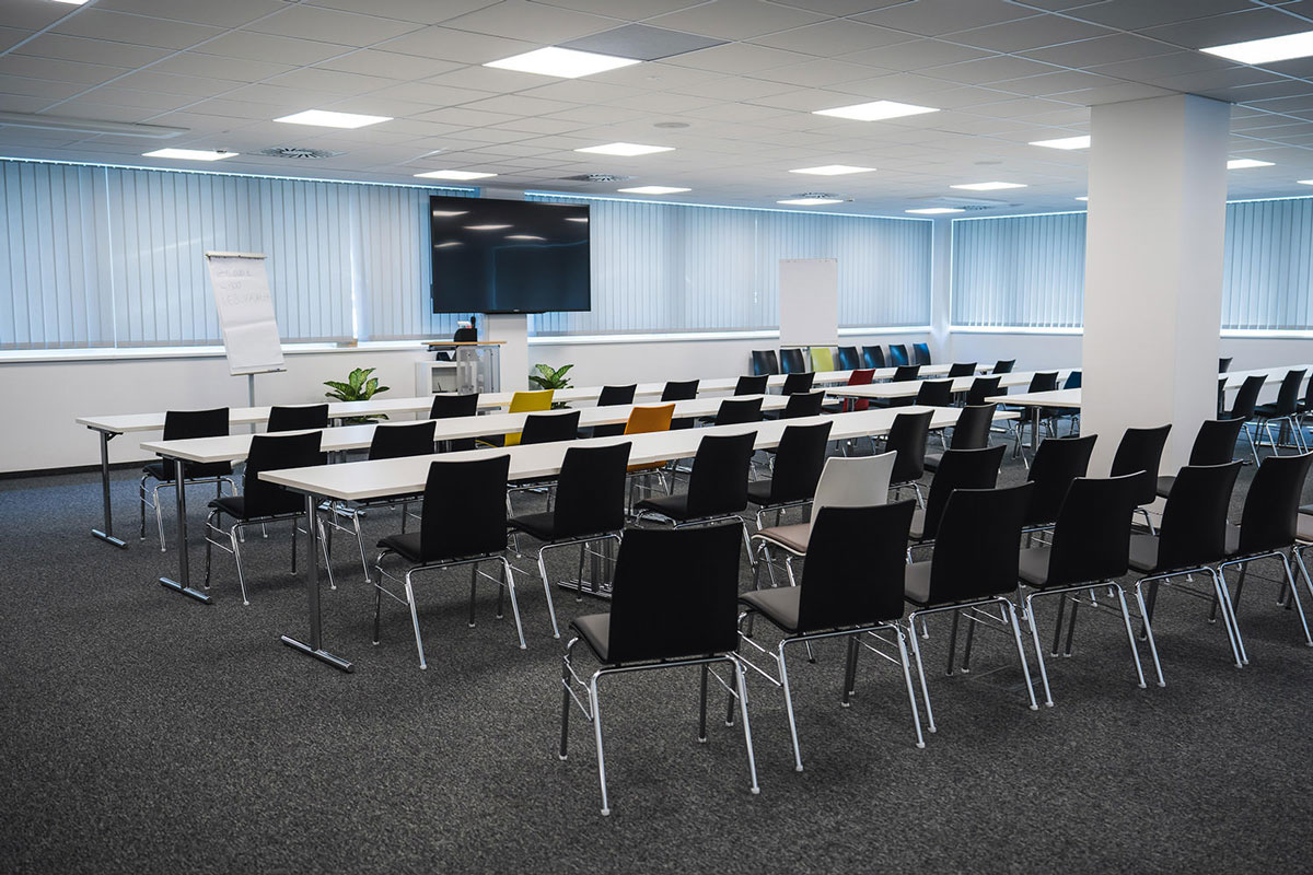 Konferenzraum im Technopark Raaba mit Reihen von Stühlen, Tischen und großer Leinwand.