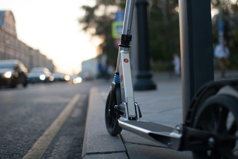 Elektroroller am Straßenrand bei Sonnenuntergang, in städtischer Umgebung mit vorbeifahrenden Autos.