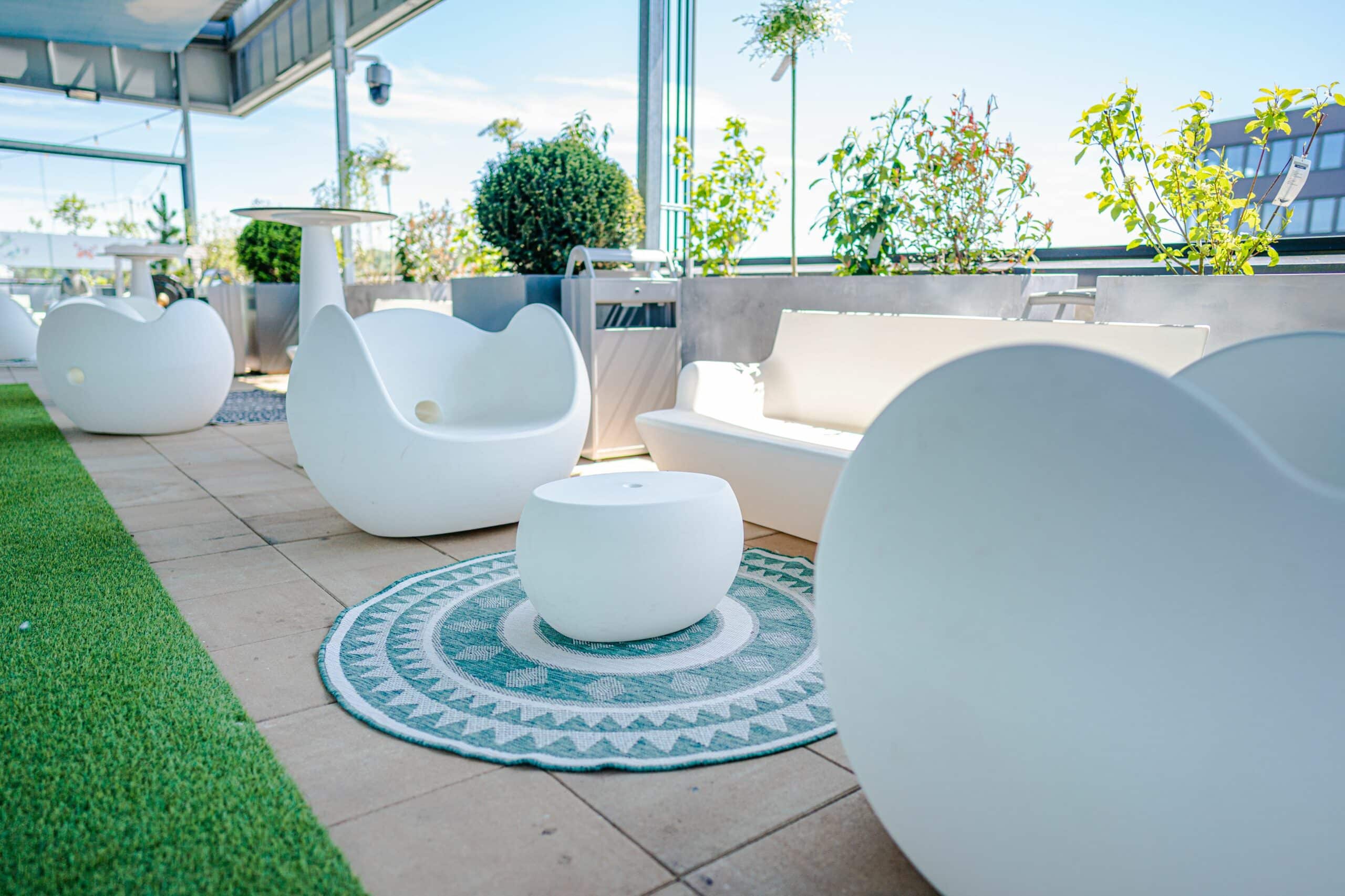 Moderne Lounge-Möbel auf sonniger Dachterrasse mit Grünpflanzen und Blick über Technopark Raaba.